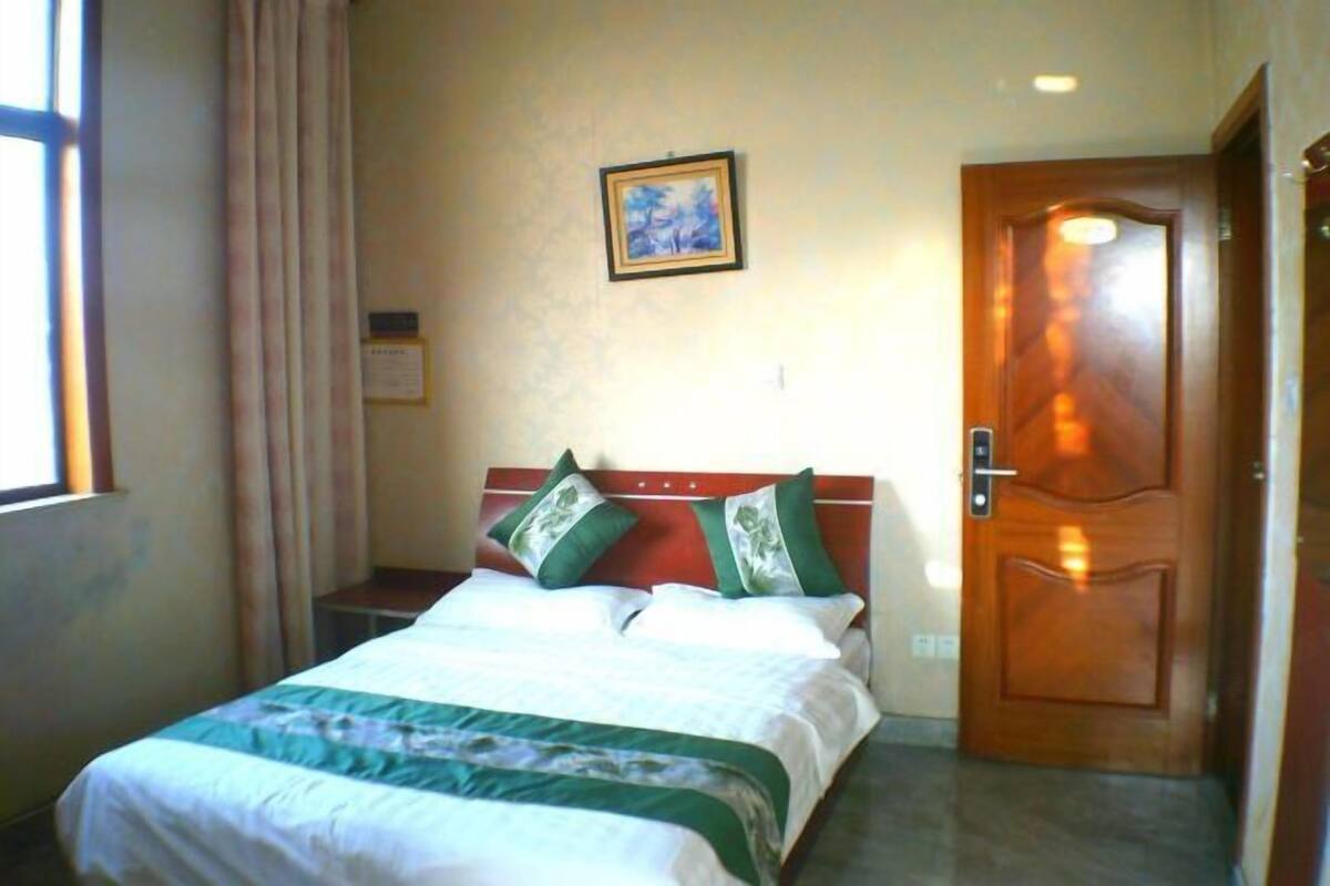 Ein Hotelzimmer mit einem Bett, einer Tür, einem Fenster mit Vorhängen und einem Wandbild.