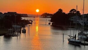 Een jachthaven met aan wal liggende boten, een zonsondergang boven het water en gebouwen op de achtergrond.