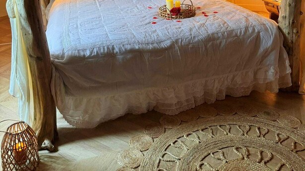 Une chambre à coucher chaleureuse et rustique, dotée d’un lit à baldaquin, de poutres en bois et d’un tapis tissé.