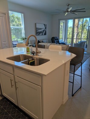 A modern kitchen with a large island, stainless steel sink, and a ceiling fan. - Charming 3-bedroom condo with AC, WiFi in lovely Punta Gorda (Punta Gorda)