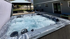 A hot tub in a backyard with a covered patio, a wooden deck, and a two-story house in the background. - 5BR Indianapolis Fun Home Arcade games & Gameroom (Indianapolis)