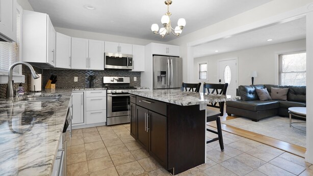 A modern kitchen with a large island, stainless steel appliances, and a dining area with a dark leather couch. - 5BR Indianapolis Fun Home Arcade games & Gameroom (Indianapolis)