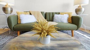 A green sofa with white and yellow cushions, a beige throw blanket, and a gold decorative plant in a white pot. - 5BR Indianapolis Fun Home Arcade games & Gameroom (Indianapolis)