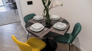 A dining table set with white plates, glasses, and cutlery, surrounded by two green chairs and one yellow chair.