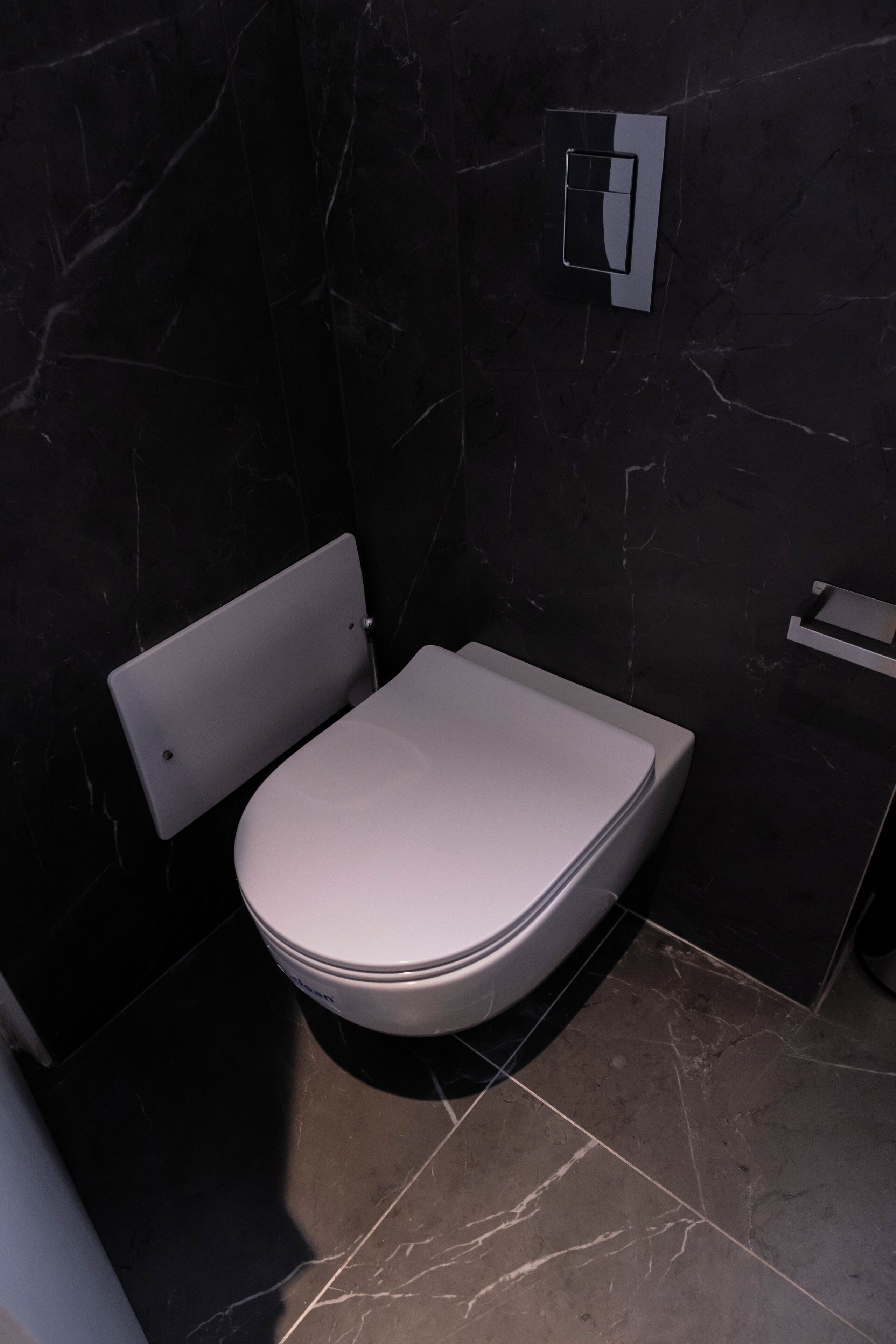 A modern bathroom with a white toilet, dark marble walls, and a small shelf.