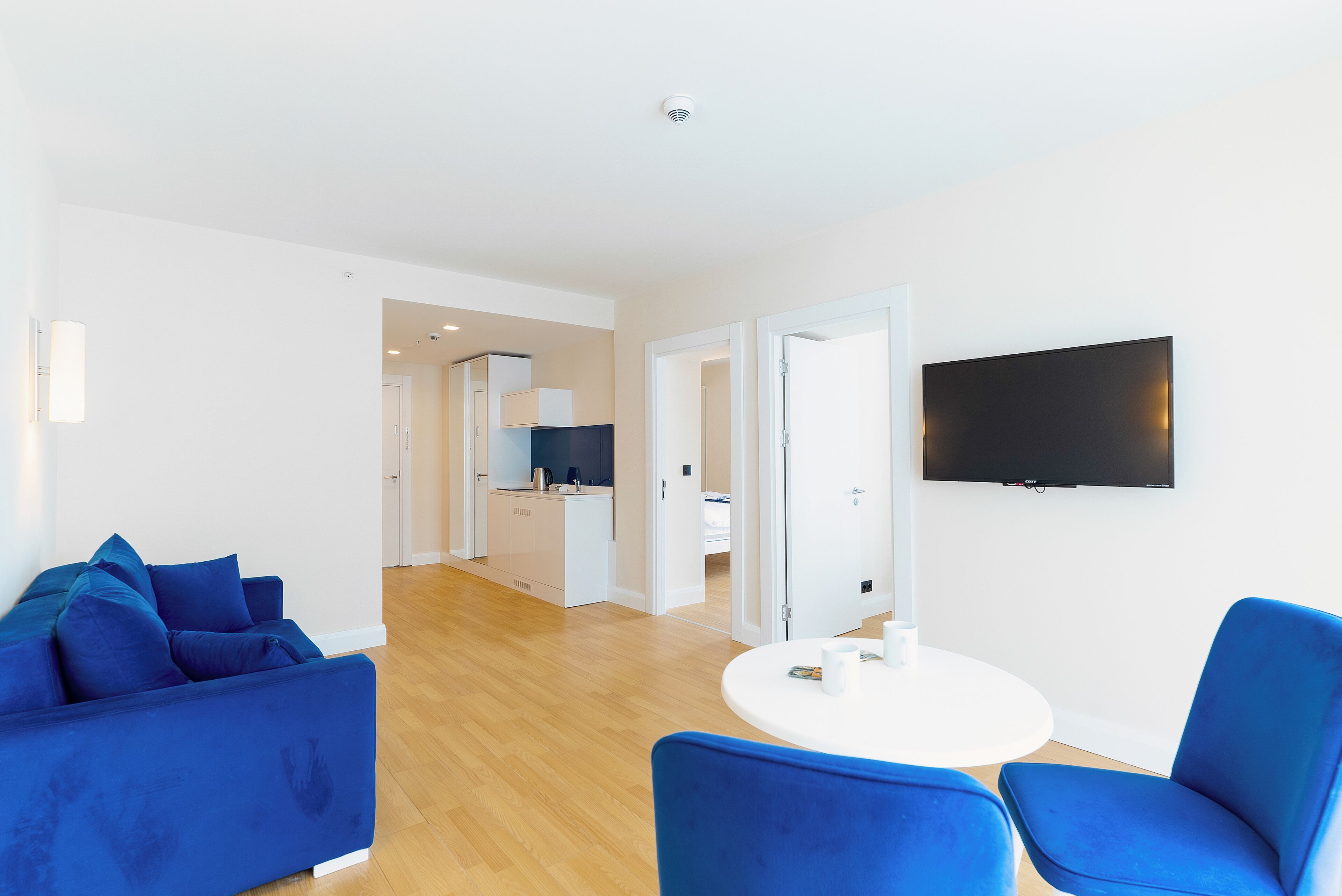 Ein modernes Wohnzimmer mit einer blauen Sofagarnitur, einem runden weißen Tisch und einem flachbildfernseher an der Wand.