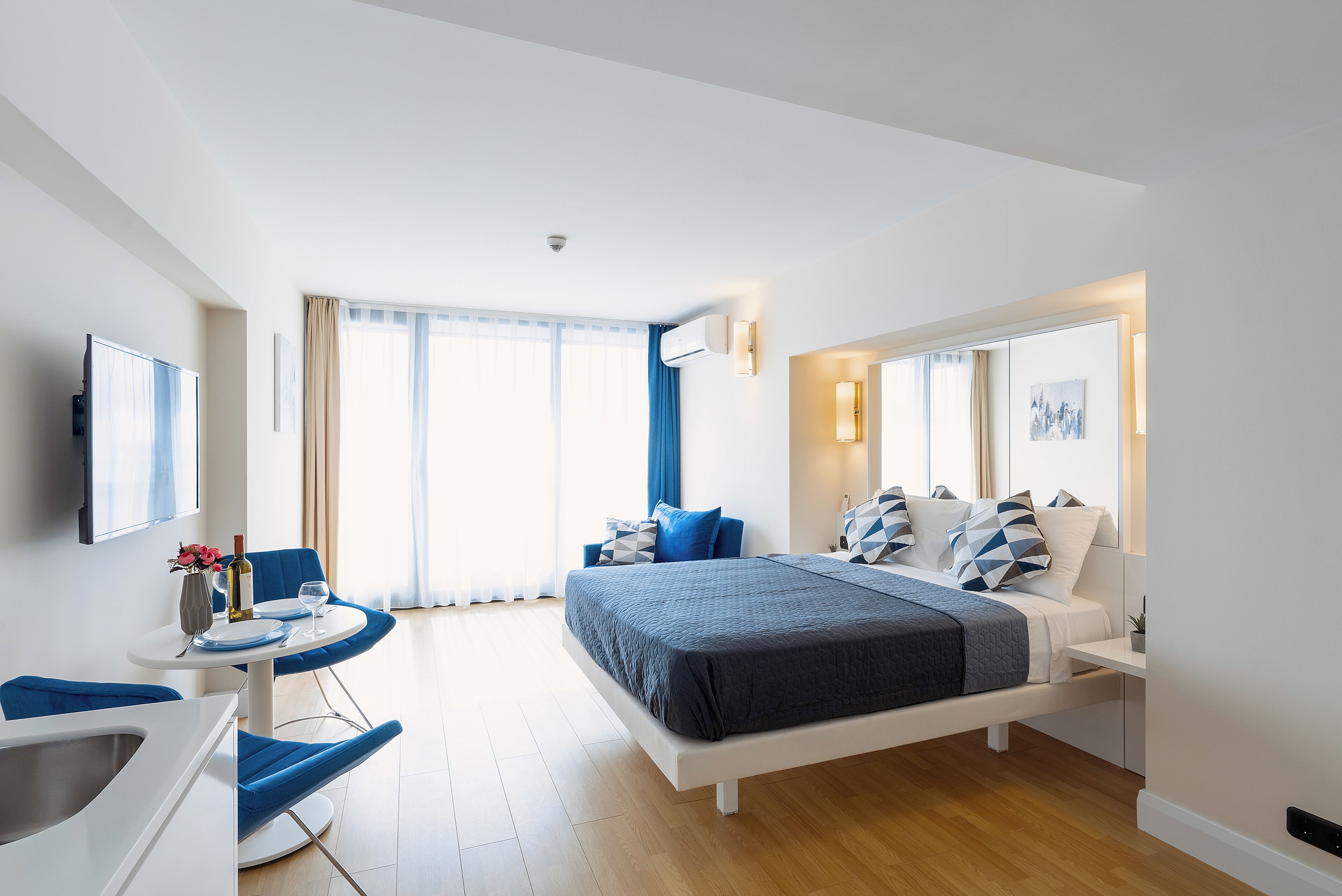 A modern hotel room with a large bed, a desk with a chair, a TV, and a window with curtains.