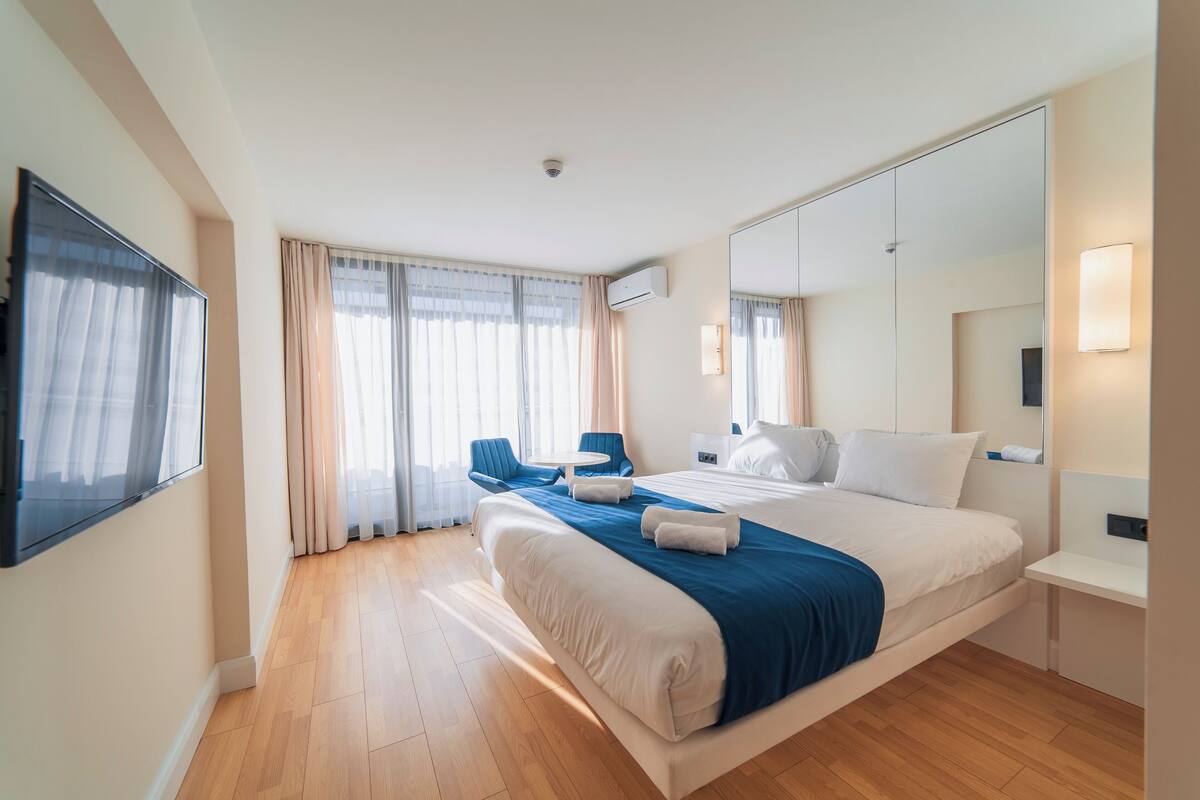 A hotel room with a large bed, a desk, a chair, and a TV.