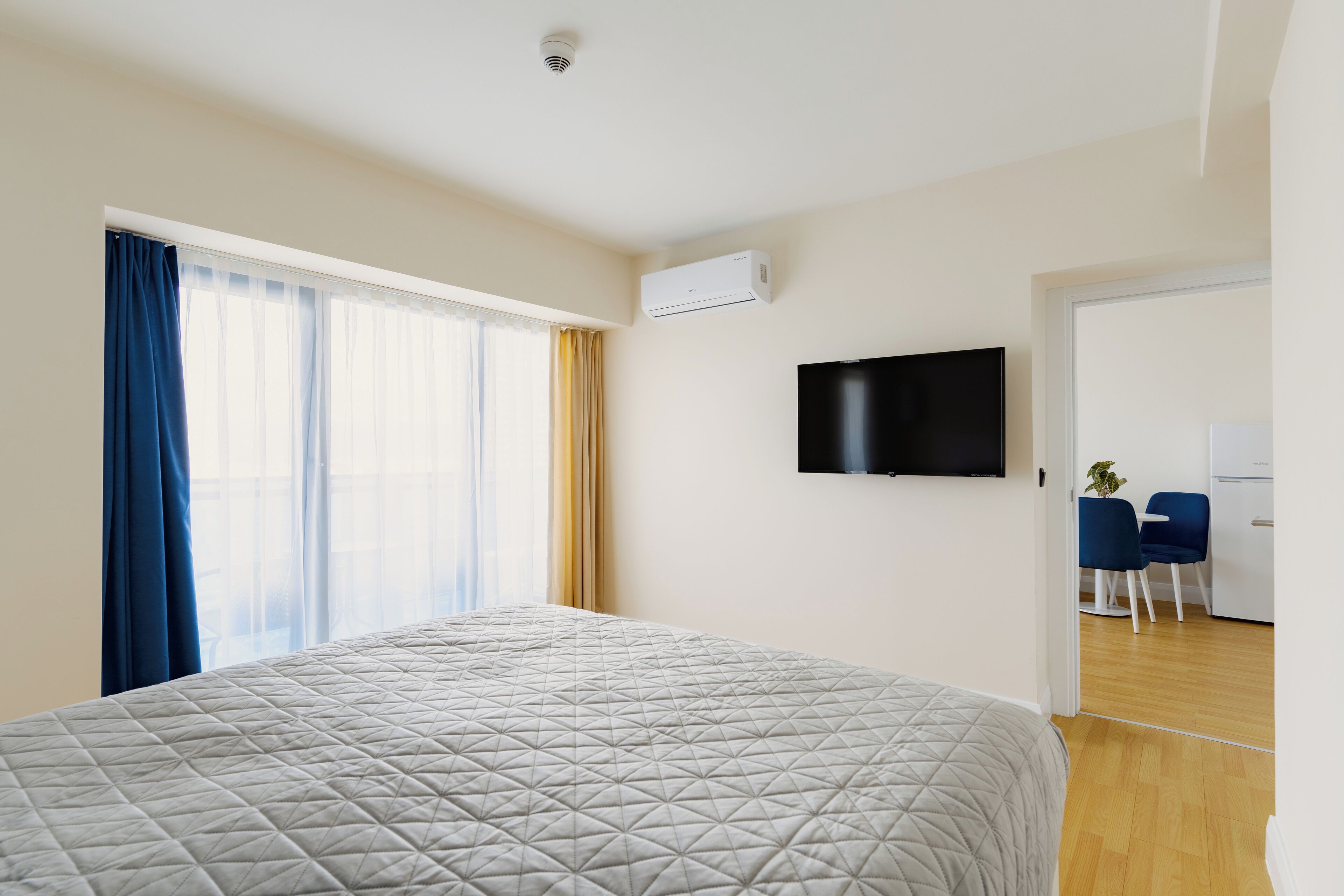 A hotel room with a bed, a TV mounted on the wall, and a desk with chairs.