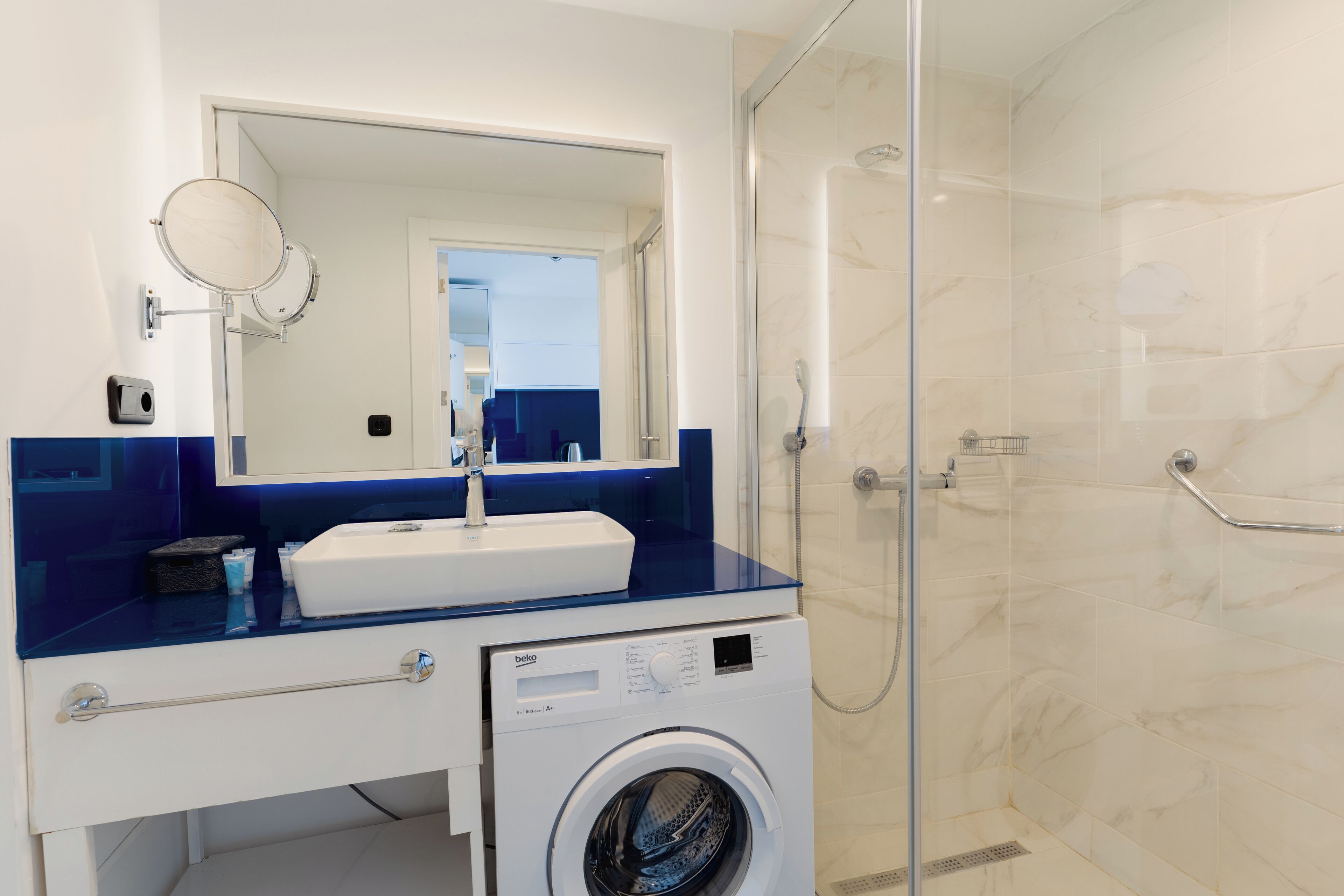 Une salle de bain moderne avec une douche à parois de verre, un lave-linge encastré et un grand miroir au-dessus du lavabo.