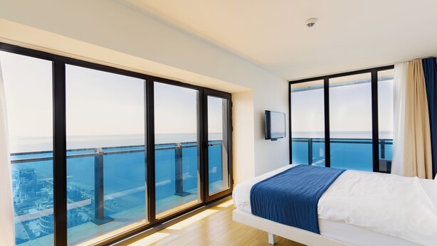 Een moderne hotelkamer met een groot balkon, een bed met een blauwe deken en een televisie aan de muur.
