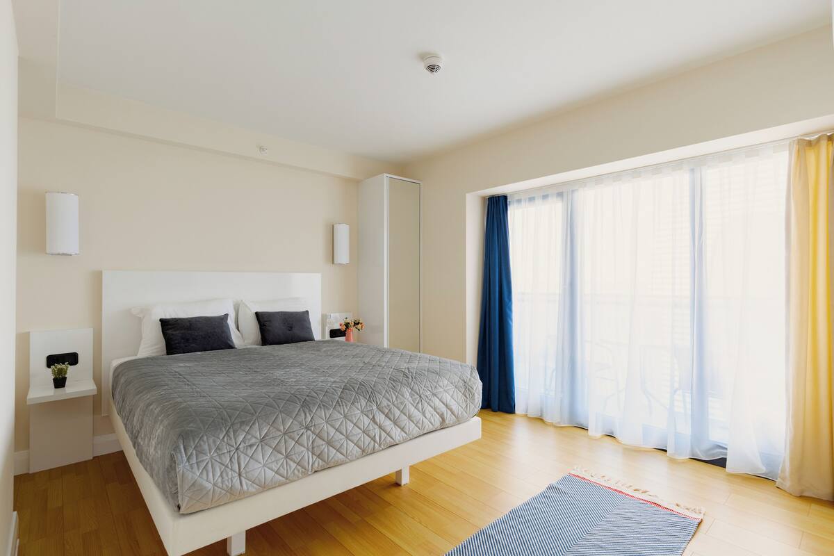 A bedroom with a bed, a bedside table, a nightstand, a window with curtains, and a ceiling light.