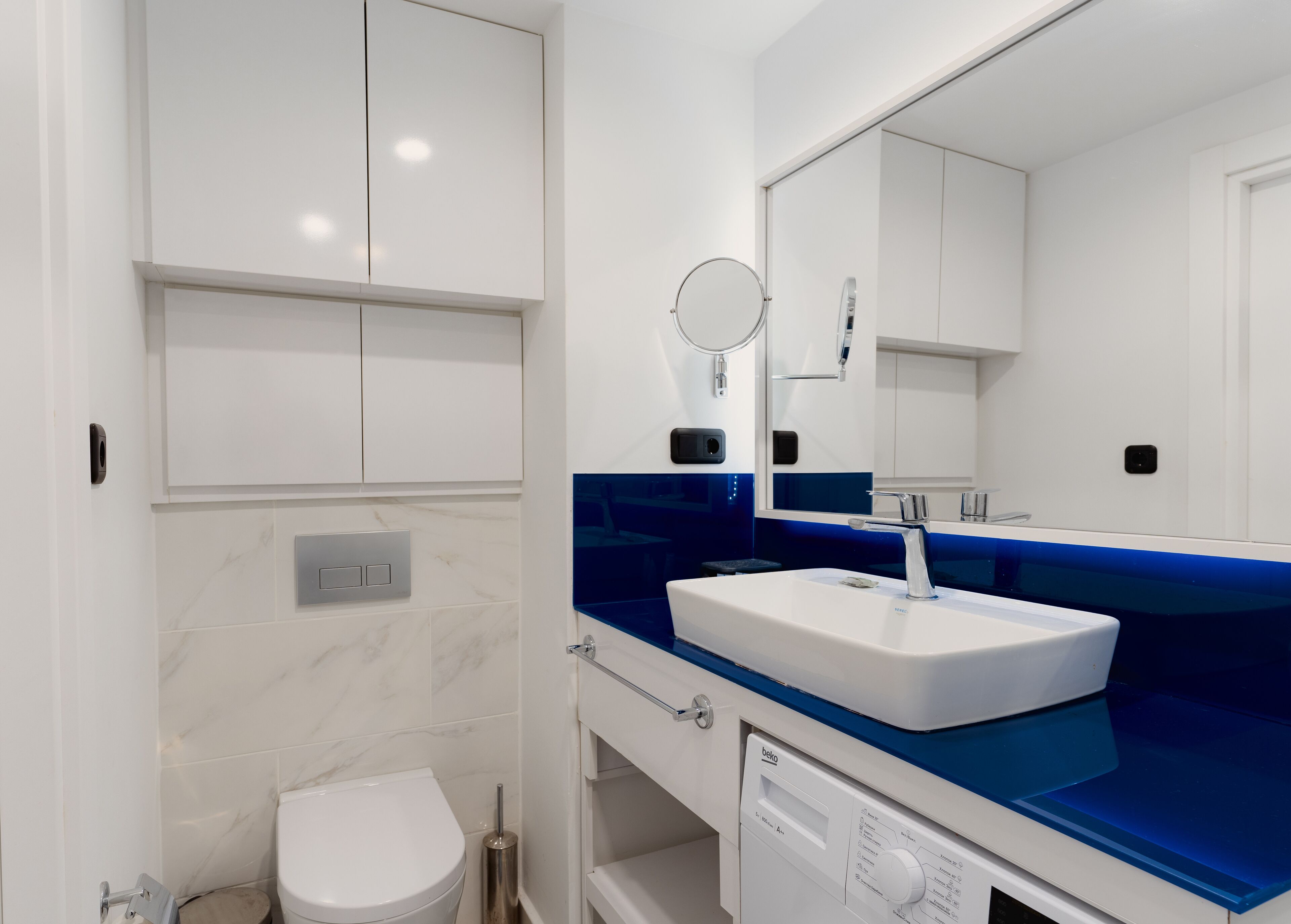 A modern bathroom with a white toilet, a white sink with a blue countertop, and a mirror above the sink.