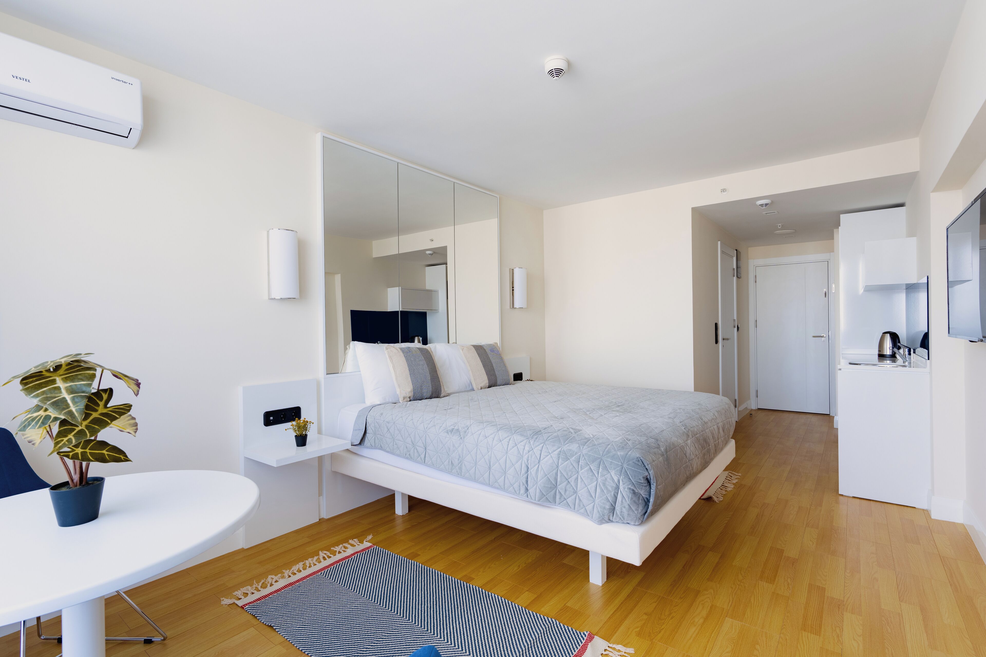 A modern bedroom with a bed, bedside tables, a desk, and a potted plant.