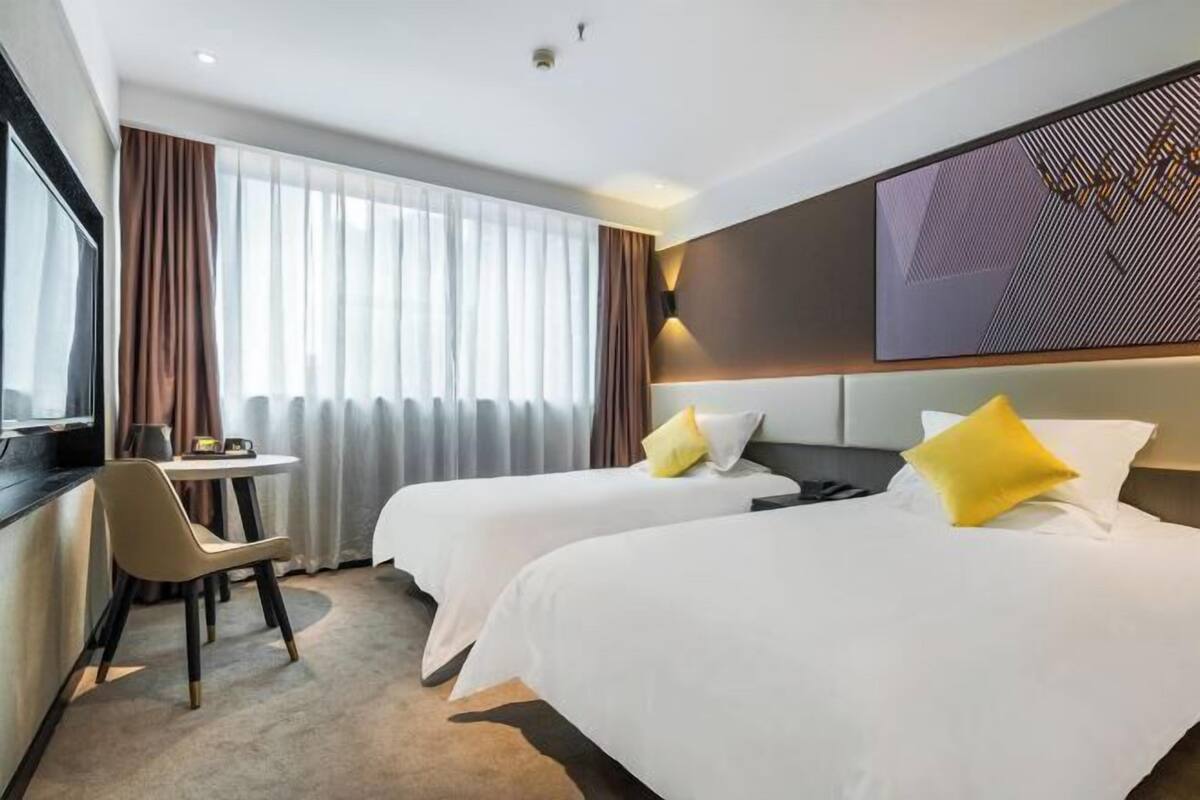 A hotel room with two beds, a desk, a chair, and a large window with curtains.