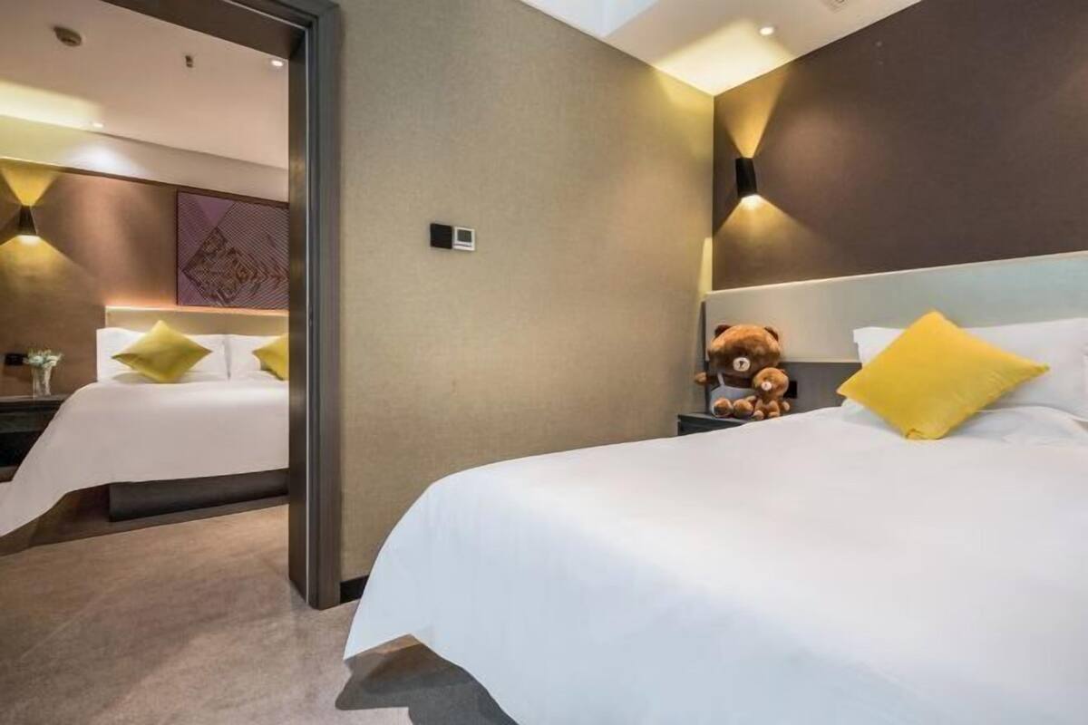 A hotel room with two beds, a teddy bear on one bed, and a lamp on the nightstand.