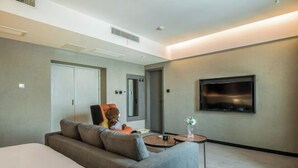 A modern hotel room with a large bed, a sofa, a small round table, a flat-screen TV mounted on the wall, and a door leading to another room. - IU Hotel (Chongqing Nanping Wanda Plaza Light Rail Station) (Chongqing)