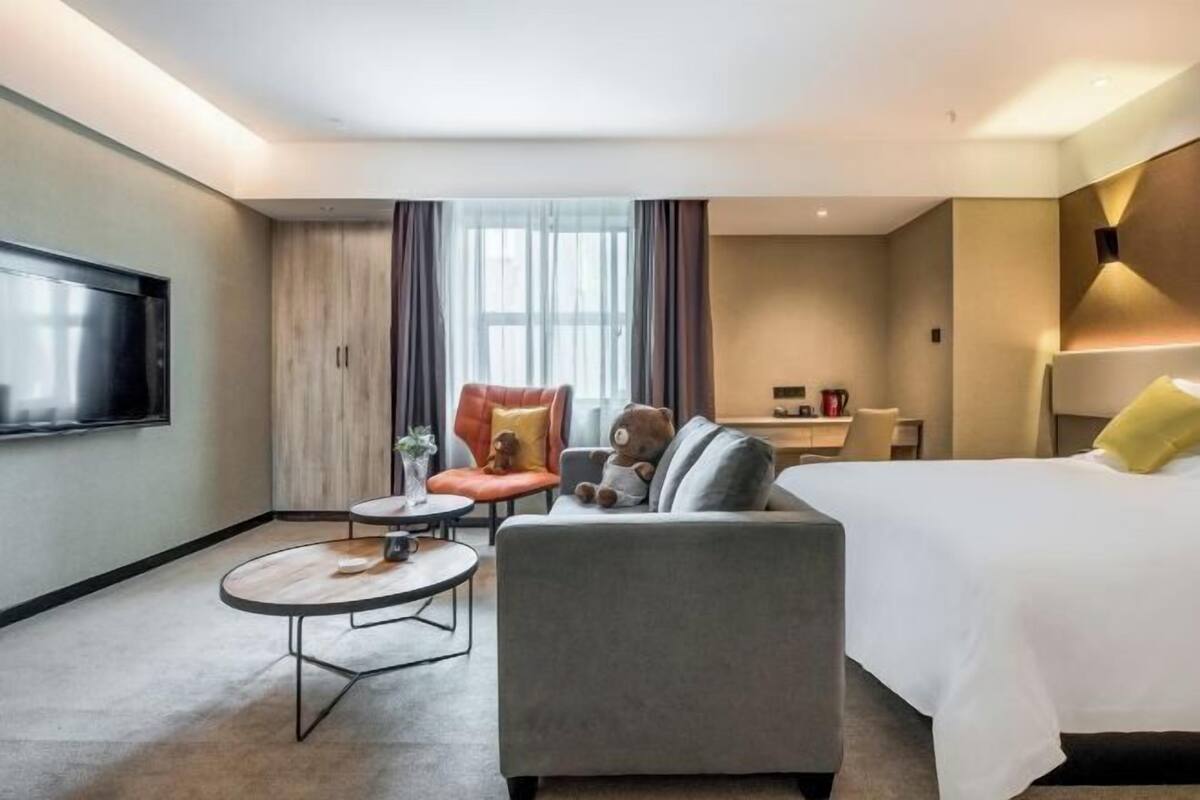A hotel room with a bed, a sofa, a chair, a small table, and a TV.
