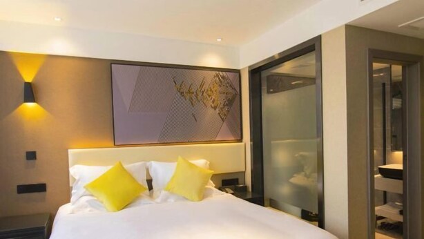 A hotel room with a large bed, a nightstand, a wall-mounted light, and a glass partition. - IU Hotel (Chongqing Nanping Wanda Plaza Light Rail Station) (Chongqing)