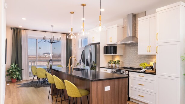 A modern kitchen with a central island, bar stools, white cabinetry, and pendant lighting.