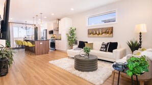 A modern living room with a sofa, coffee table, and chairs. There is a kitchen area with cabinets and a dining table.