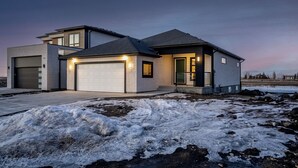A modern two-story house with a garage, a driveway, and a snow-covered ground.