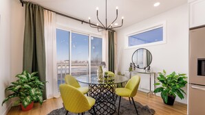 A modern dining area with a glass table, four chairs, a chandelier, and potted plants.