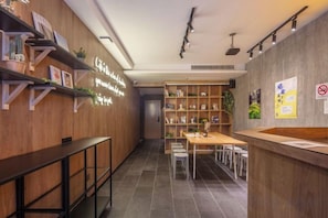 A modern interior with a reception desk, shelves with books and plants, and a dining area with chairs and tables.