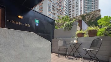 An outdoor seating area with a table and chairs, a potted plant, and a building facade with signage.