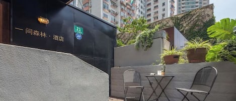 An outdoor seating area with a table and chairs, a potted plant, and a building facade with signage.