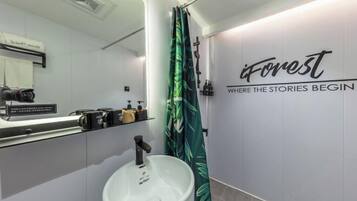 Un baño moderno con un lavamanos blanco, un espejo, una cortina de ducha con estampado de hojas y un cartel en la pared que dice 'iForest WHERE THE STORIES BEGIN'.