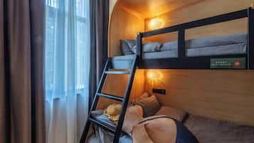 Una cama litera con escalera, una lámpara fijada a la pared y una ventana con cortinas.