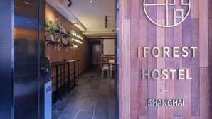 Η είσοδος του IFOREST HOSTEL στη Σαγκάη, με μια ξύλινη πρόσοψη και έναν μοντέρνο εσωτερικό χώρο που διαθέτει σκάλα και ράφια με φυτά.