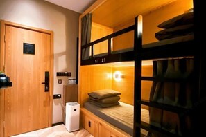 Habitación con literas, una puerta de madera, un electrodoméstico pequeño blanco y una lámpara fijada a la pared.