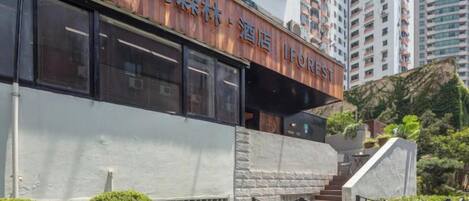 A hotel with a modern facade, a staircase leading to the entrance, and a view of surrounding high-rise buildings.