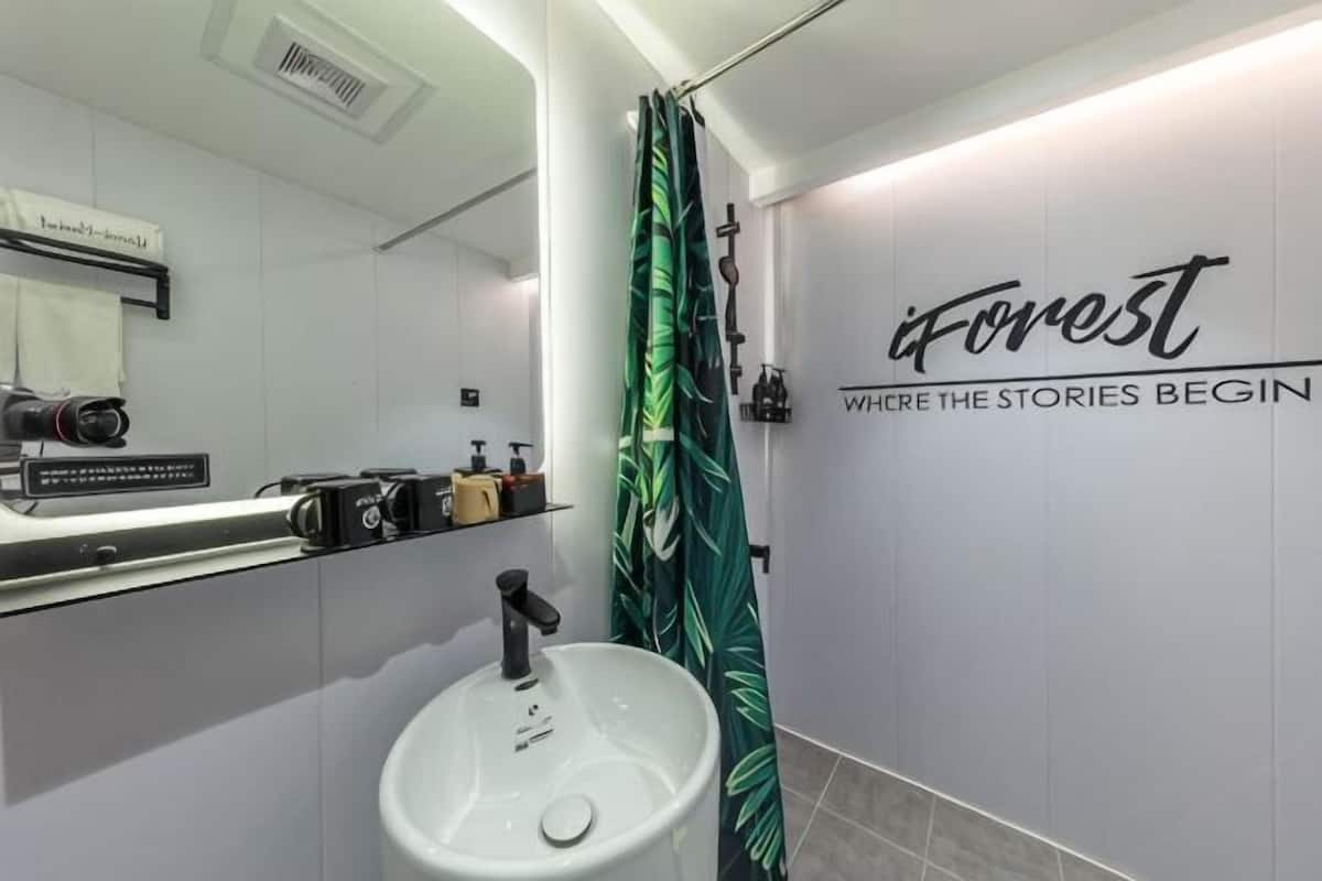 A bathroom with a white sink, a mirror, a shower curtain with a leaf pattern, and a wall with the text 'iForest' and 'Where the stories begin.'