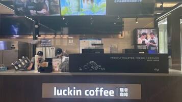 A coffee shop interior with a counter displaying 'luckin coffee' signage, a coffee machine, and a television screen above the counter.