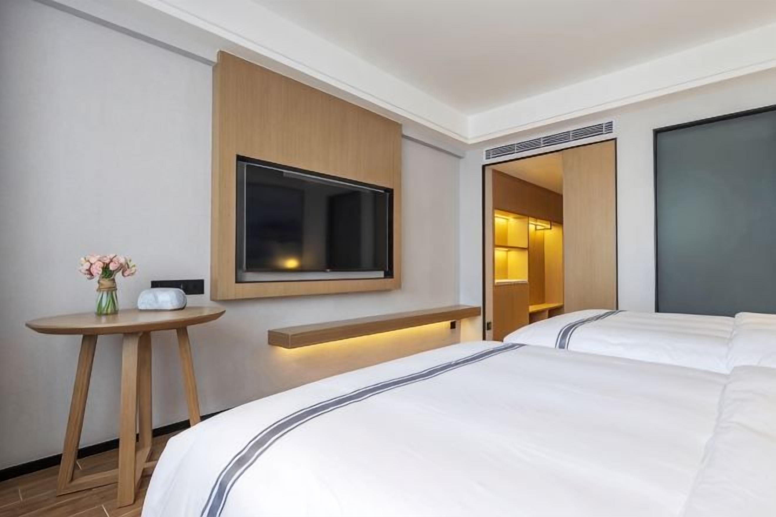 A hotel room with a bed, a bedside table with a vase, a mounted TV, and a built-in shelf.
