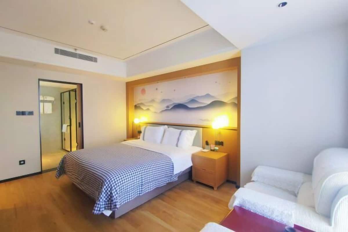 A hotel room with a bed, bedside table, lamp, and a painting on the wall.