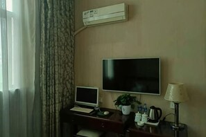 A hotel room with a desk, a flat-screen TV, a laptop, a potted plant, a lamp, and an air conditioning unit. - Zhengzhou Xinyang Lingrui Building Hotel (Provincial People's Hospital Metro Station) (Zhengzhou)