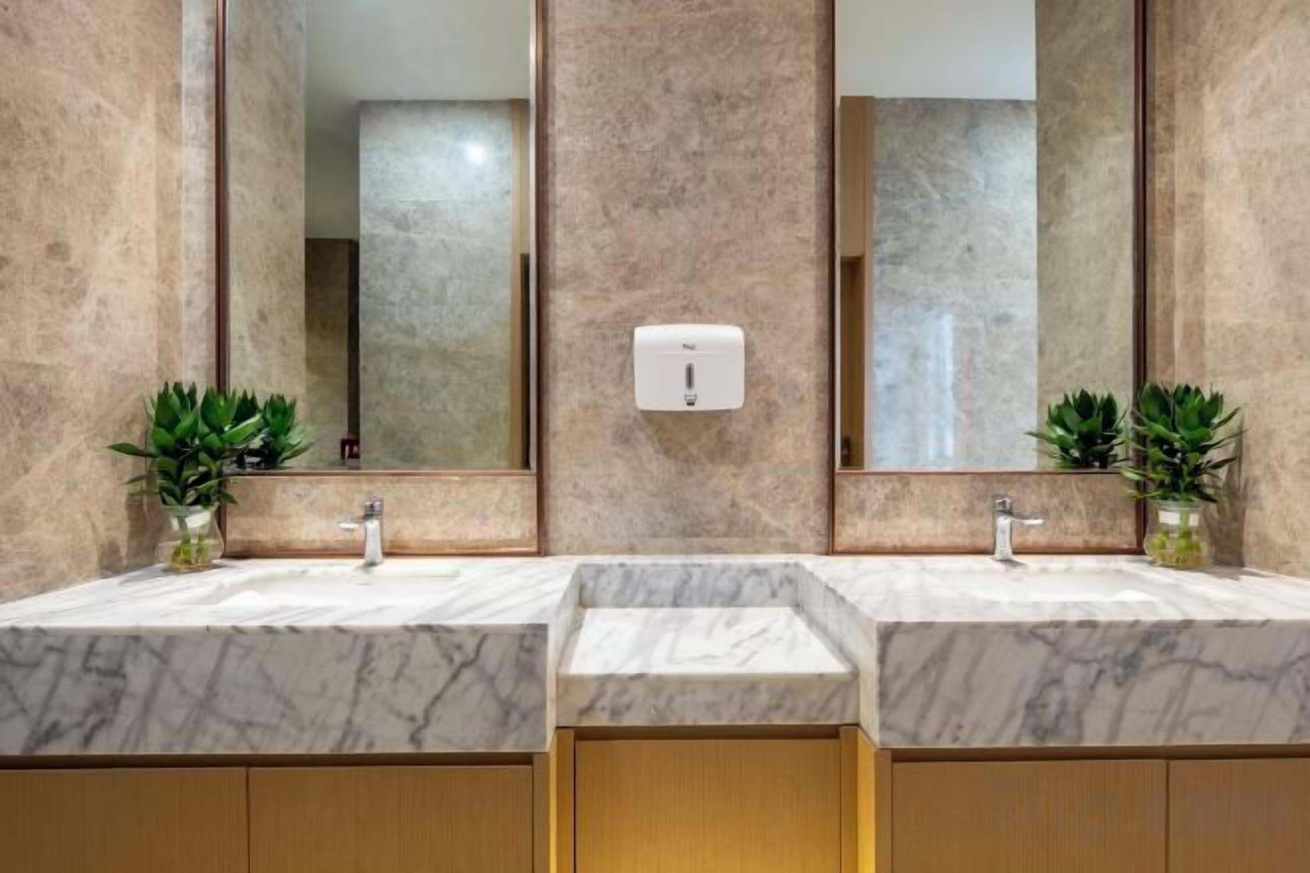 Une salle de bain avec deux vasques, des plans de travail en marbre, des meubles en bois et deux plantes en pot.