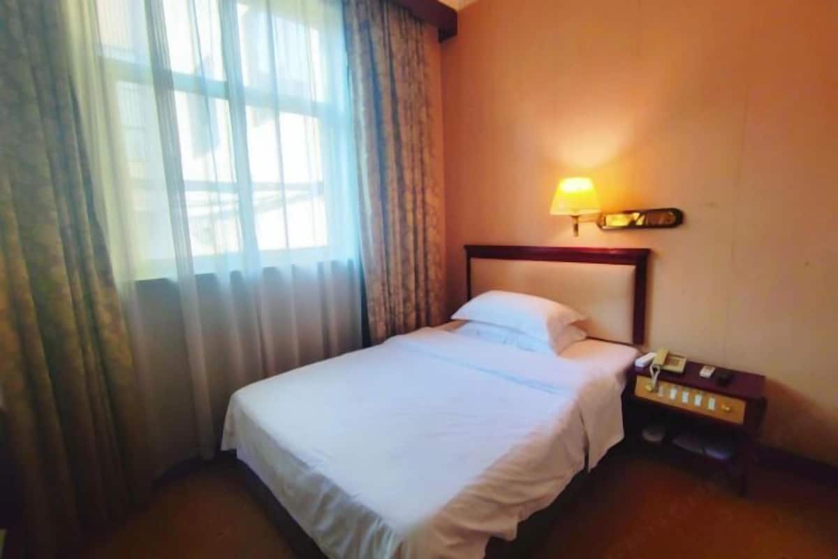 A hotel room with a bed, a nightstand, a lamp, and a window with curtains.
