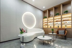 A modern reception area with a curved white sofa, a round table, and a shelving unit displaying books and plants. - Zhengzhou Xinyang Lingrui Building Hotel (Provincial People's Hospital Metro Station) (Zhengzhou)