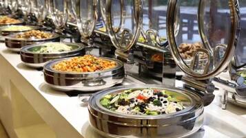 A buffet line with multiple food stations, each with a metal bowl and a glass lid.