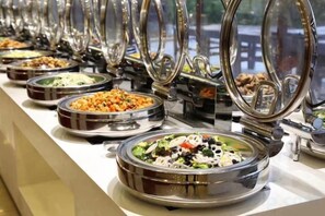 Un buffet proposant différents plats, présentés sur plusieurs tables, chacune étant équipée d’un récipient en métal et d’un couvercle en verre.