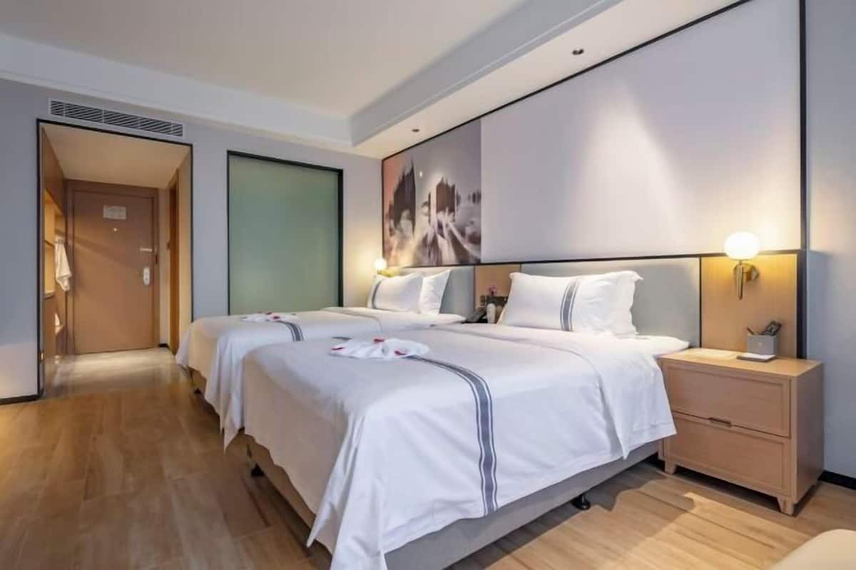 A hotel room with a large bed, bedside tables, a wardrobe, and a door leading to another room.