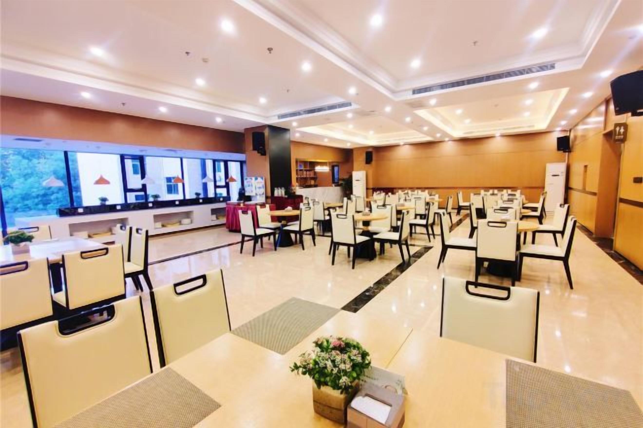 Un comedor espacioso con varias mesas y sillas, una barra con caja registradora, y un amplio ventanal con vista a árboles.