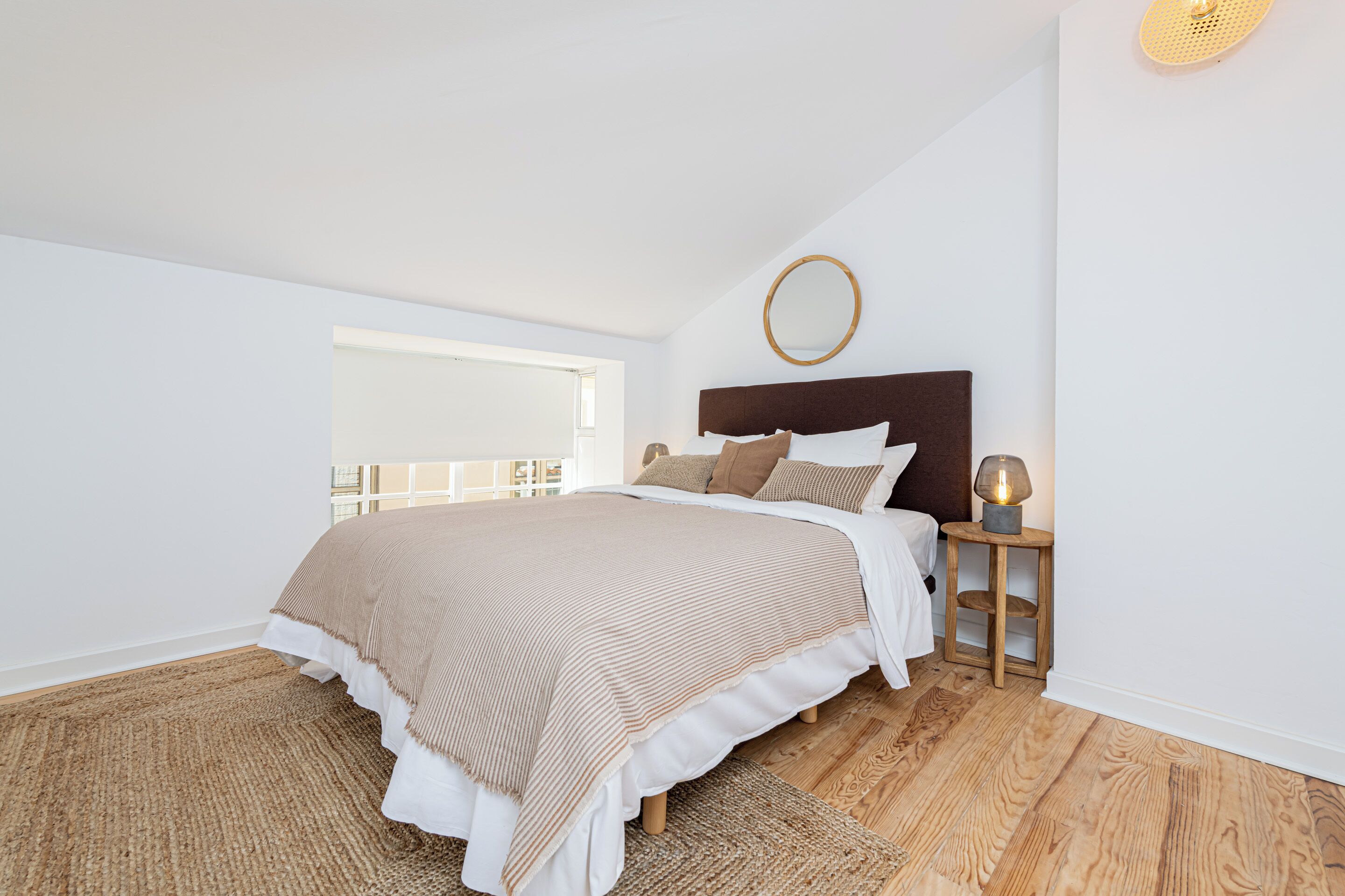 Una camera da letto con un letto grande, un comodino con una lampada, una finestra e un elemento decorativo circolare a parete.