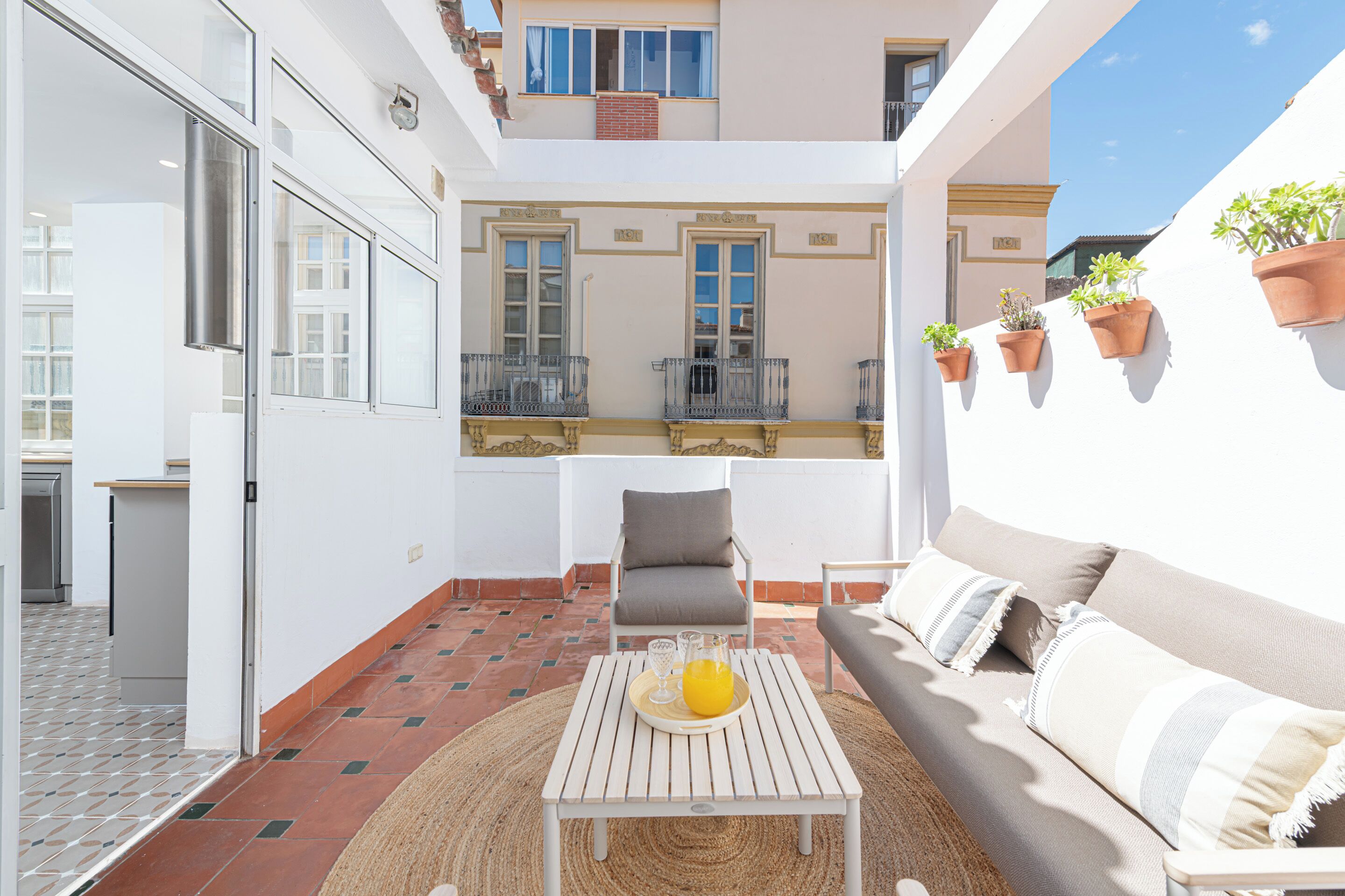 A balcony with a white table, a grey sofa, and potted plants.
