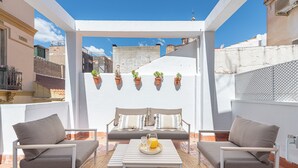 Eine Dachterrasse mit einer Couch, zwei Stühlen, einem Tisch und Topfpflanzen.